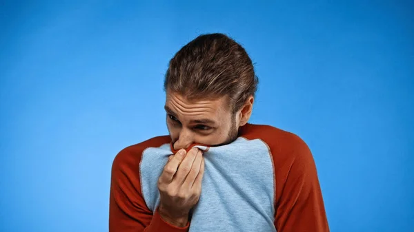 Man covering nose with shirt while feeling unpleasant smell on blue — Stock Photo