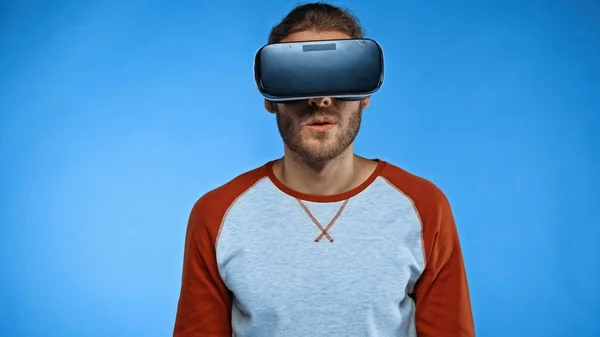 Hombre barbudo en auriculares de realidad virtual sobre fondo azul - foto de stock