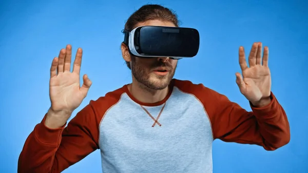 Junger Mann im Virtual-Reality-Headset gestikuliert auf blauem Grund — Stockfoto
