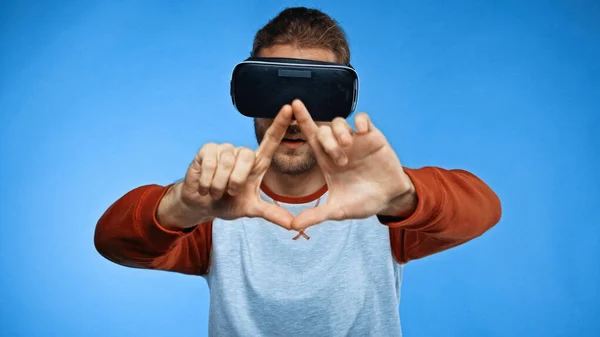 Бородатий молодий чоловік у гарнітурі віртуальної реальності жестикулює на синьому — стокове фото