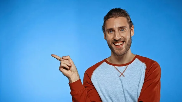 Junger fröhlicher Mann zeigt mit Finger auf blau — Stockfoto