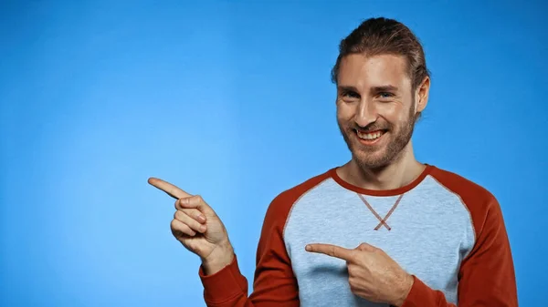 Junger fröhlicher Mann zeigt mit den Fingern auf blau — Stockfoto