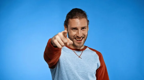 Smiling young man pointing with finger while looking at camera on blue — Stock Photo