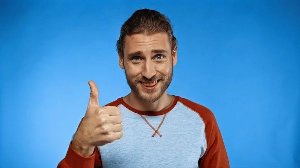 Smiling young man showing thumb up while looking at camera on blue — Stock Photo
