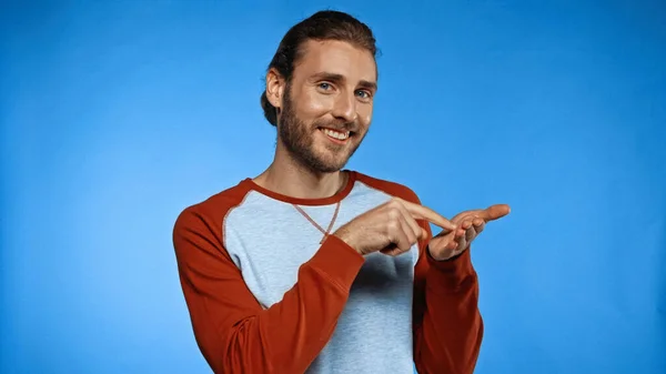 Excited young man pointing with finger at hand while showing text me gesture on blue — Stock Photo