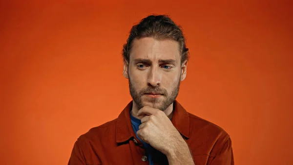 Thoughtful man touching beard on orange background — Stock Photo