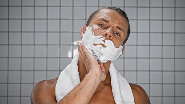 Hombre sin camisa aplicando espuma de afeitar en el baño - foto de stock