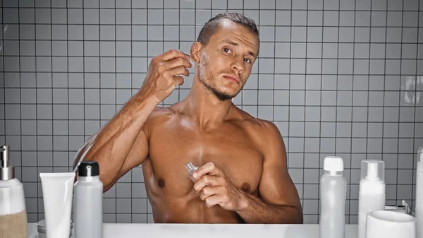 Hombre sin camisa sosteniendo la botella y aplicando suero en el baño - foto de stock
