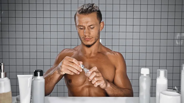 Hemdloser Mann hält Flasche mit Serum im Badezimmer — Stockfoto