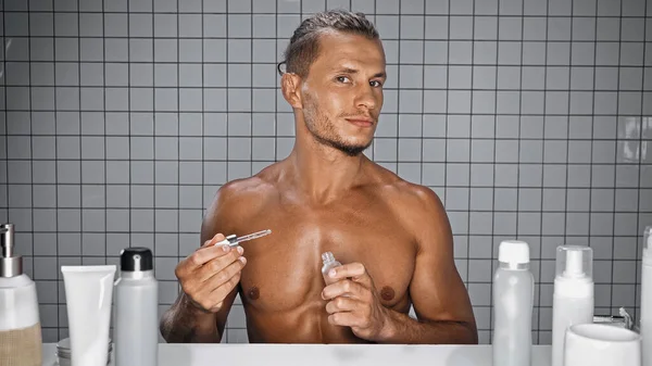 Giovane uomo senza camicia bottiglia con siero e pipetta in bagno — Foto stock