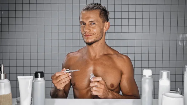 Hemdloser Mann hält Flasche mit Serum und Pipette im Badezimmer — Stockfoto