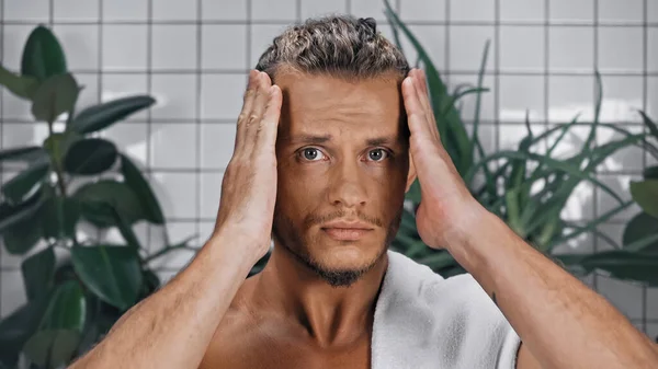 Homme torse nu ajuster les cheveux près de plantes vertes sur fond flou dans la salle de bain — Photo de stock