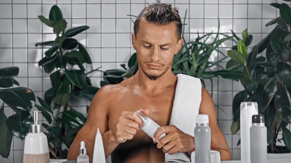 Без сорочки чоловік тримає пляшку з піною для гоління біля зелених рослин на розмитому фоні у ванній — стокове фото