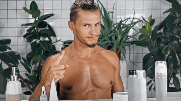 Shirtless man pointing with finger at himself while looking at camera near green plants on blurred background in bathroom — Stock Photo