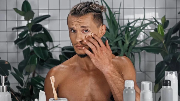 Homme torse nu touchant visage près de plantes vertes sur fond flou dans la salle de bain — Photo de stock