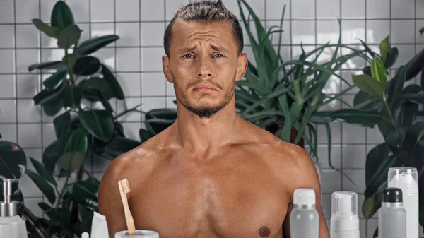 Sad shirtless man near green plants on blurred background in bathroom — Stock Photo