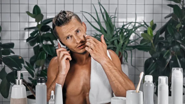 Bärtiger Mann spricht auf Smartphone im Badezimmer mit Pflanzen auf verschwommenem Hintergrund — Stockfoto