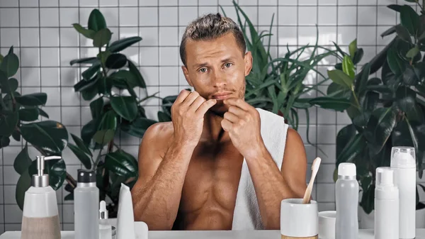 Bearded man flossing teeth in bathroom near green plants on blurred background — Stock Photo