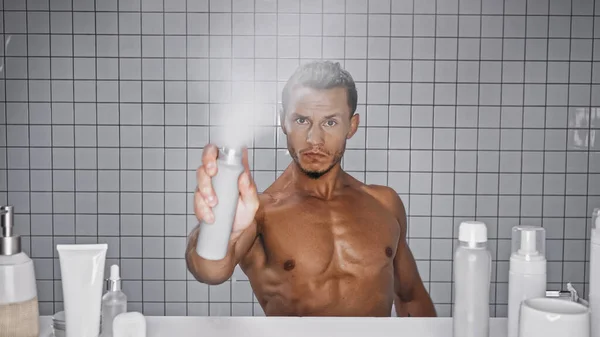 Homem muscular segurando garrafa enquanto pulverizando desodorizante no banheiro — Fotografia de Stock