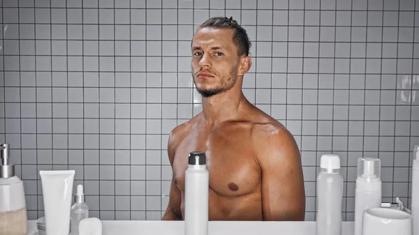 М'язистий чоловік стоїть біля пляшок у ванній — стокове фото