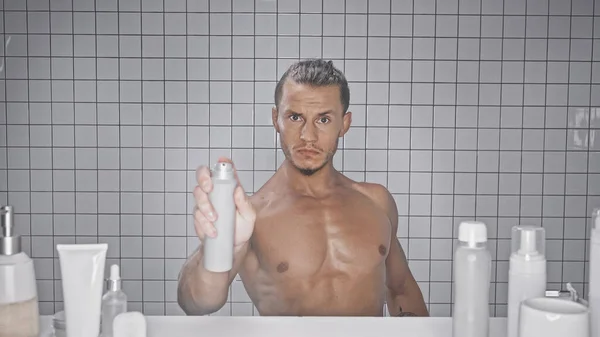 Homem muscular segurando garrafa com desodorizante no banheiro — Fotografia de Stock