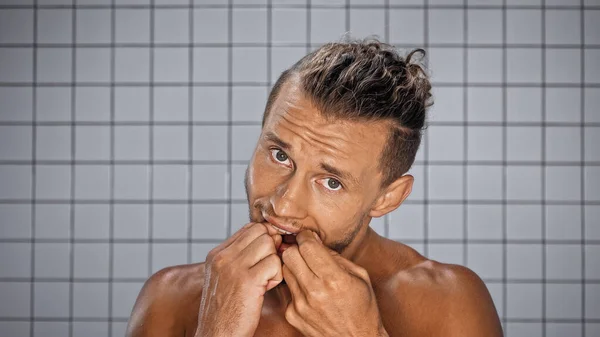 Uomo barbuto guardando la fotocamera mentre i denti filo interdentale in bagno — Foto stock