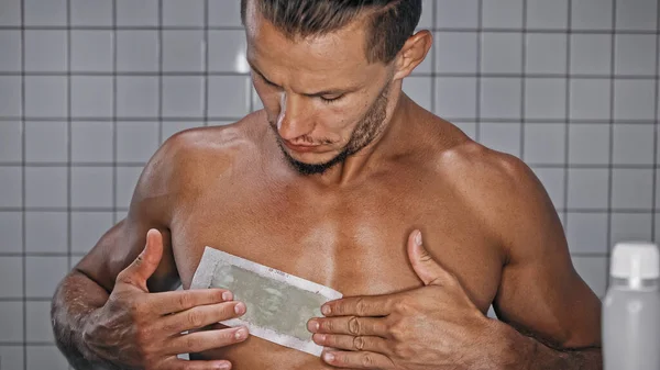 Homme torse nu appliquant bande de cire sur la poitrine dans la salle de bain — Photo de stock