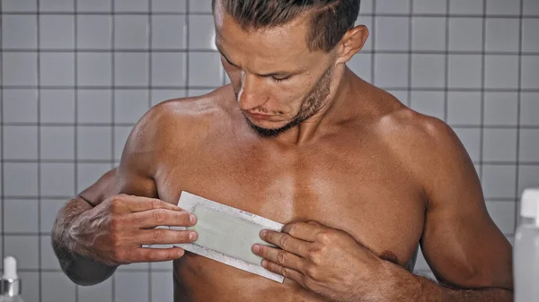 Bärtiger Mann trägt Wachsstreifen auf Brust im Badezimmer auf — Stockfoto