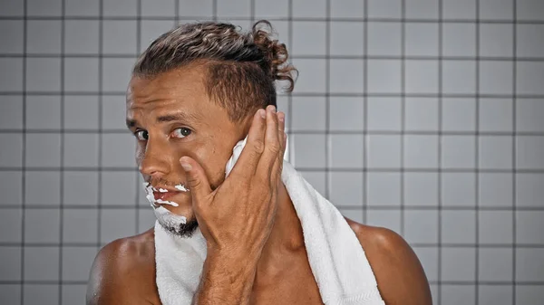 Homme barbu appliquant mousse à raser sur le visage dans la salle de bain — Photo de stock