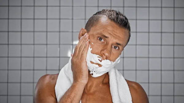 Hemdloser Mann trägt Rasierschaum im modernen Badezimmer auf — Stockfoto