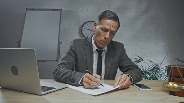 Insurance agent writing on paper near devices and scales on blurred foreground — Stock Photo