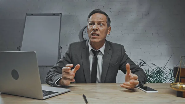 Aggressive insurance agent looking away near devices and scales on blurred foreground on table — Stock Photo