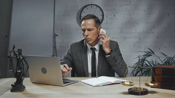 Insurance agent talking on smartphone near laptop, notebook and statuette of justice — Stock Photo