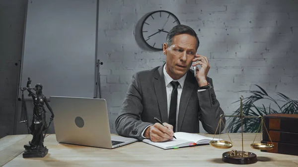 Agente assicurativo che parla su smartphone vicino a laptop, notebook e bilance sul tavolo in ufficio — Foto stock