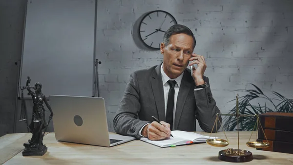 Insurance agent talking on smartphone near laptop, notebook and scales on table in office — Stock Photo