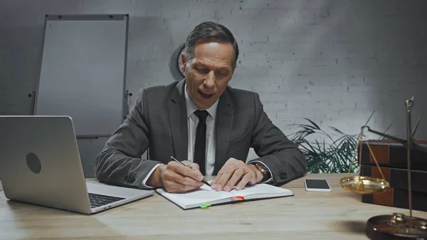 Insurance agent writing on notebook near devices, scales and books — Stock Photo