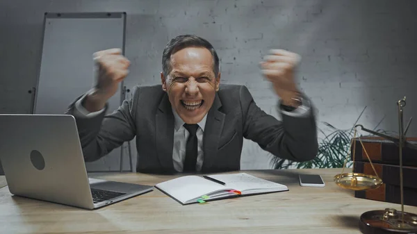 Сердитий страховий агент, що показує кулаки біля пристроїв, ноутбуків і ваг на розмитому передньому плані — стокове фото