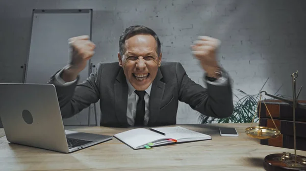 Angry insurance agent showing fists near devices, notebook and scales on blurred foreground — Stock Photo