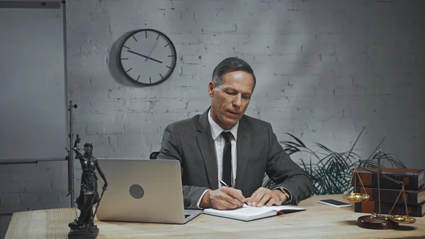 Agente de seguros escribiendo en un cuaderno mientras trabaja cerca de dispositivos y escalas - foto de stock