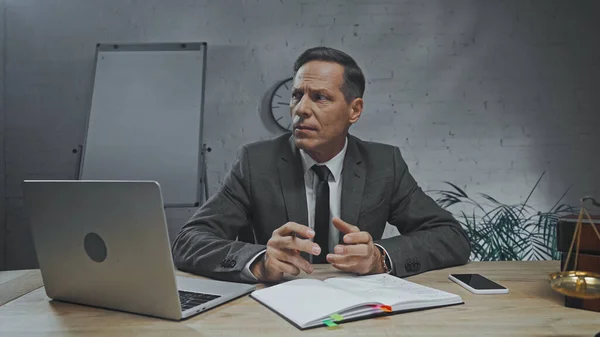 Insurance agent holding pen and looking away near devices and notebook on table — Stock Photo