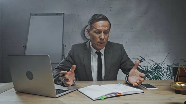 Worried insurance agent looking at notebook near devices and scales on blurred foreground — Stock Photo