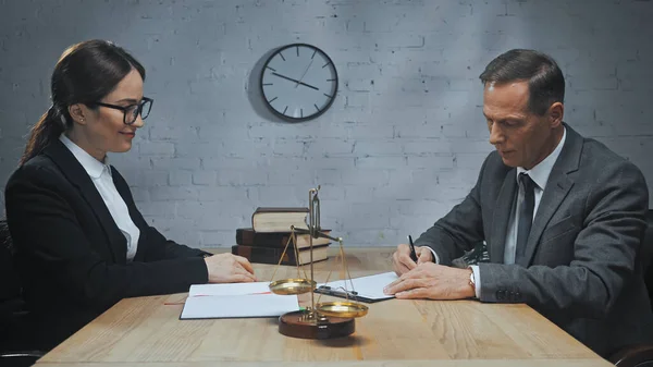 Insurance agent writing on document near colleague, notebook and scales in office — Stock Photo