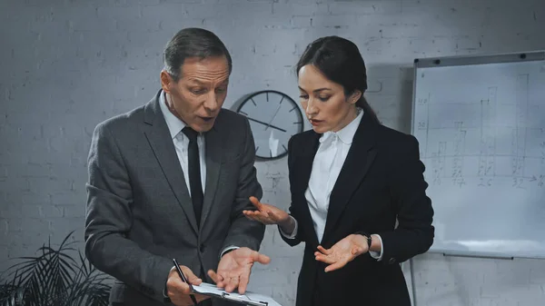 Insurance agent pointing at clipboard near colleague in office — Stock Photo