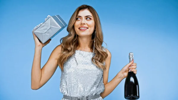 Happy woman holding gift box and bottle of champagne isolated on blue — Stock Photo