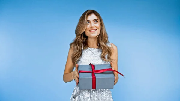 Neugierige Frau hält verpackten Geschenkkarton in der Hand und lächelt auf blau — Stockfoto