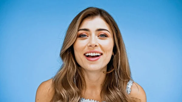 Mujer asombrada con el pelo ondulado mirando a la cámara y sonriendo aislado en azul - foto de stock