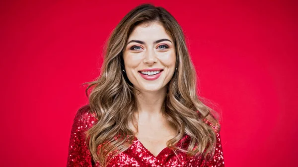 Femme heureuse avec les cheveux ondulés regardant la caméra isolée sur rouge — Photo de stock