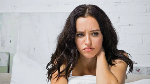 Bouleversé jeune femme toucher le cou tout en étant assis dans la chambre — Photo de stock