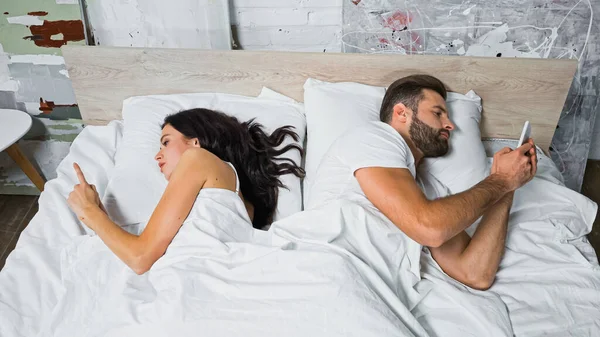 Young couple messaging on smartphones while lying in bed back to back — Stock Photo