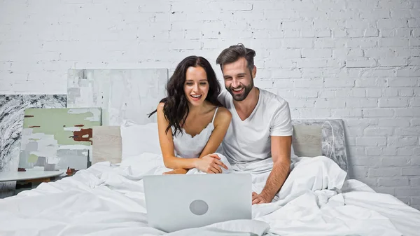 Heureux jeune couple regarder comédie sur ordinateur portable dans la chambre — Photo de stock